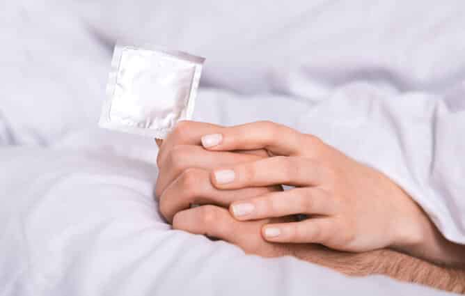 Safety sex is important in modern world. New condom in male and female hands in bed, panorama with empty space