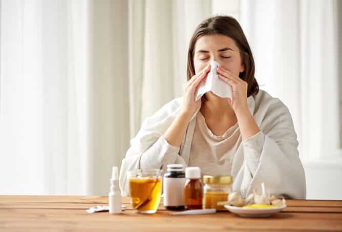 health care, flu, hygiene, age and people concept - sick woman with medicine blowing nose to paper wipe at home