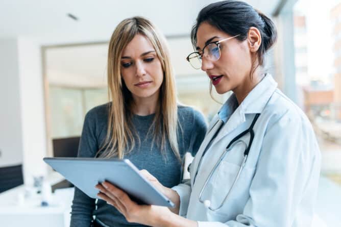 Shot of beautiful female doctor talking while explaining medical treatment with digital tablet to patient in the consultation.