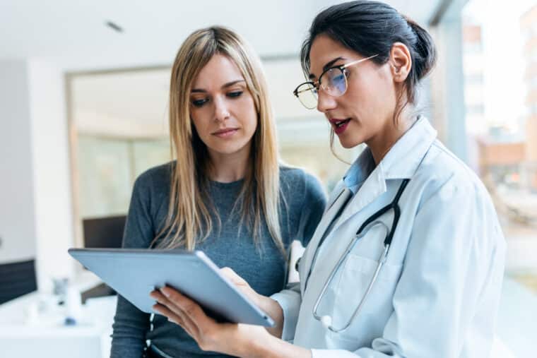 Shot of beautiful female doctor talking while explaining medical treatment with digital tablet to patient in the consultation.