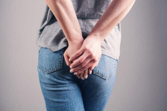 young woman has hemorrhoids against gray background