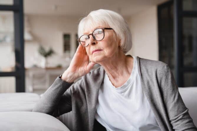 Sad tired ill sick lonely disappointed caucasian old elderly senior woman grandmother sitting on the sofa couch, feeling nostalgy, pain, missing grandchildren, bankruptcy, fraud at home