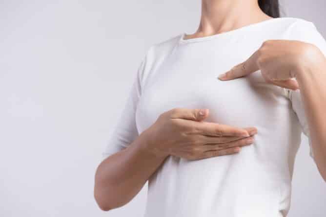 Woman hand checking lumps on her breast for signs of breast cancer on gray background. Healthcare concept.