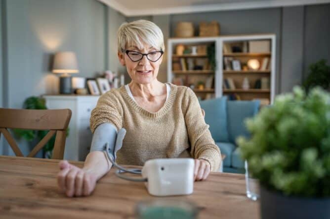 One woman senior caucasian female use blood pressure device on hand to check health results while sit at home real people health care concept